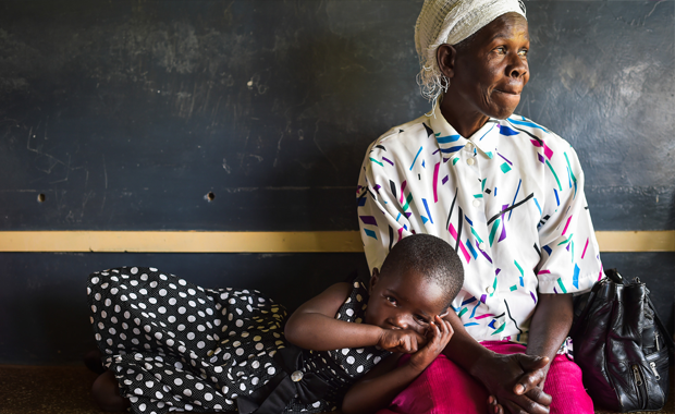 A young child lies on a waiting bench while she waits to be seen by a clinical officer at a rural health facility near the town of Kakamega, Kenya. (Credit: Tobin Jones/IntraHealth International)
